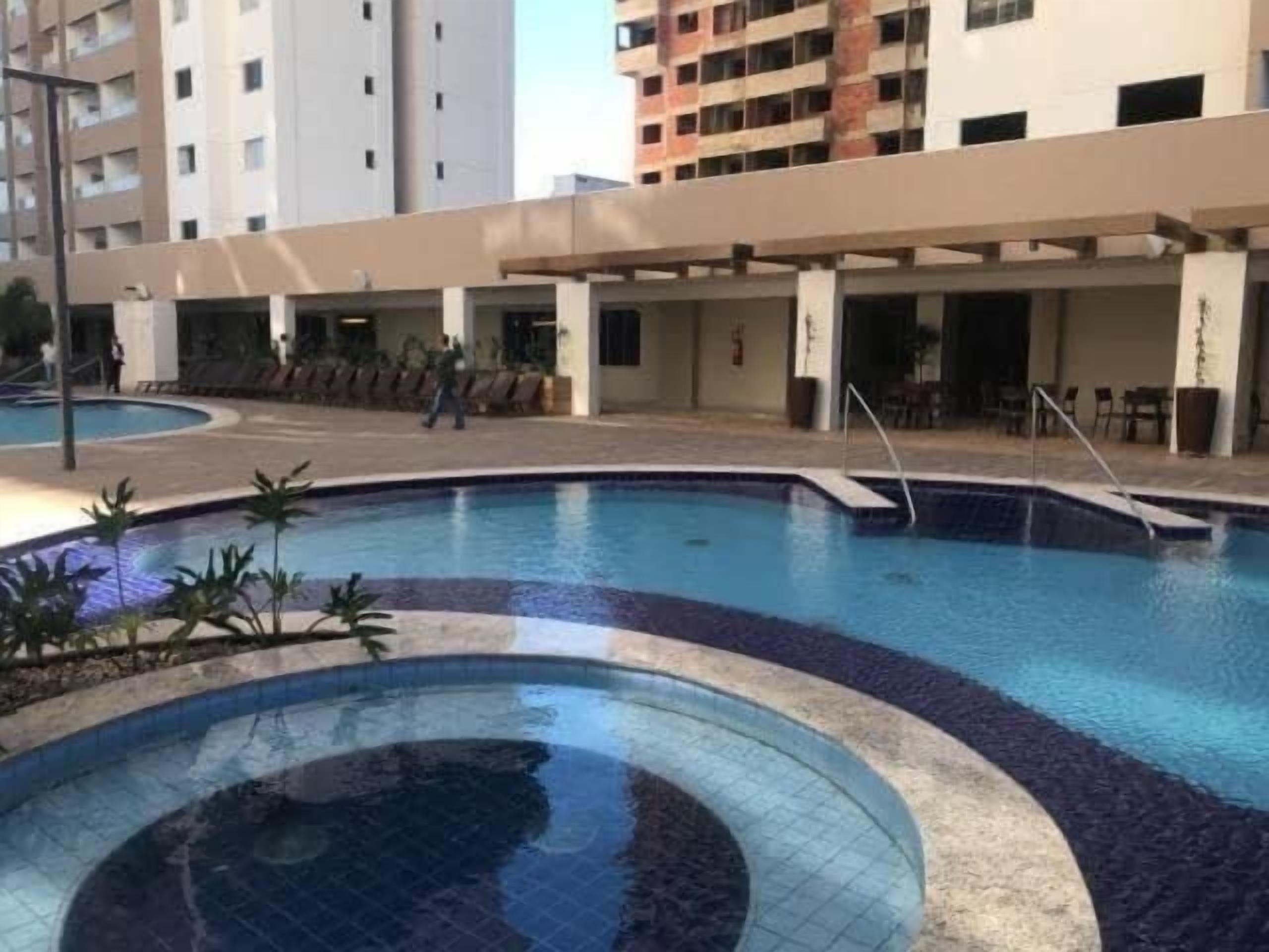 A swimming pool with a tiled edge, surrounded by a covered area with chairs and tables.