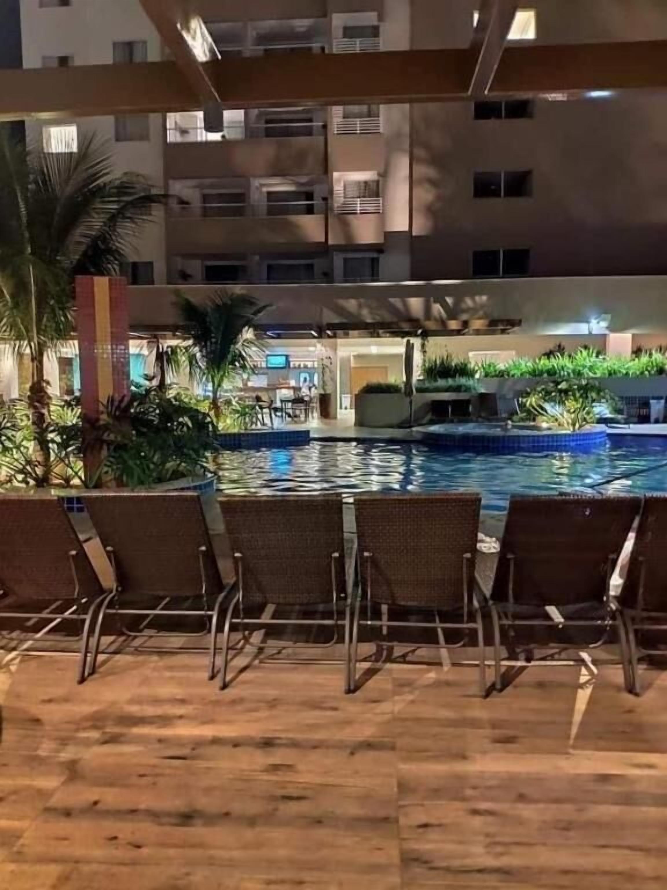 A poolside area with lounge chairs and a pool, surrounded by greenery and a building in the background.