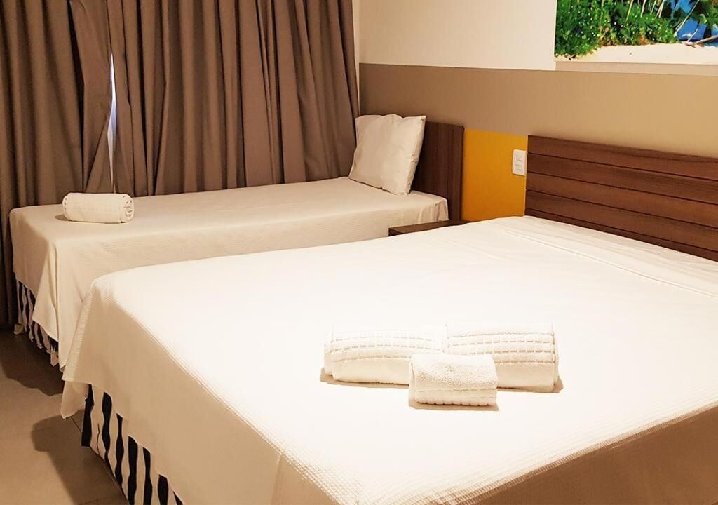 Ein Hotelzimmer mit zwei Einzelbetten, einem Holzkopfteil und einem Fenster mit Vorhängen.