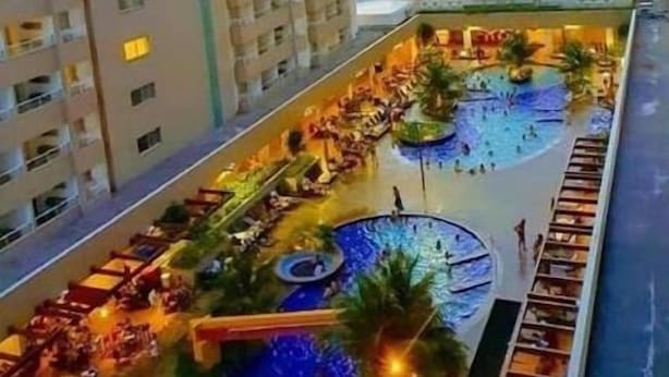 Un hotel con piscina en la azotea, varios balcones y vistas del paisaje circundante.