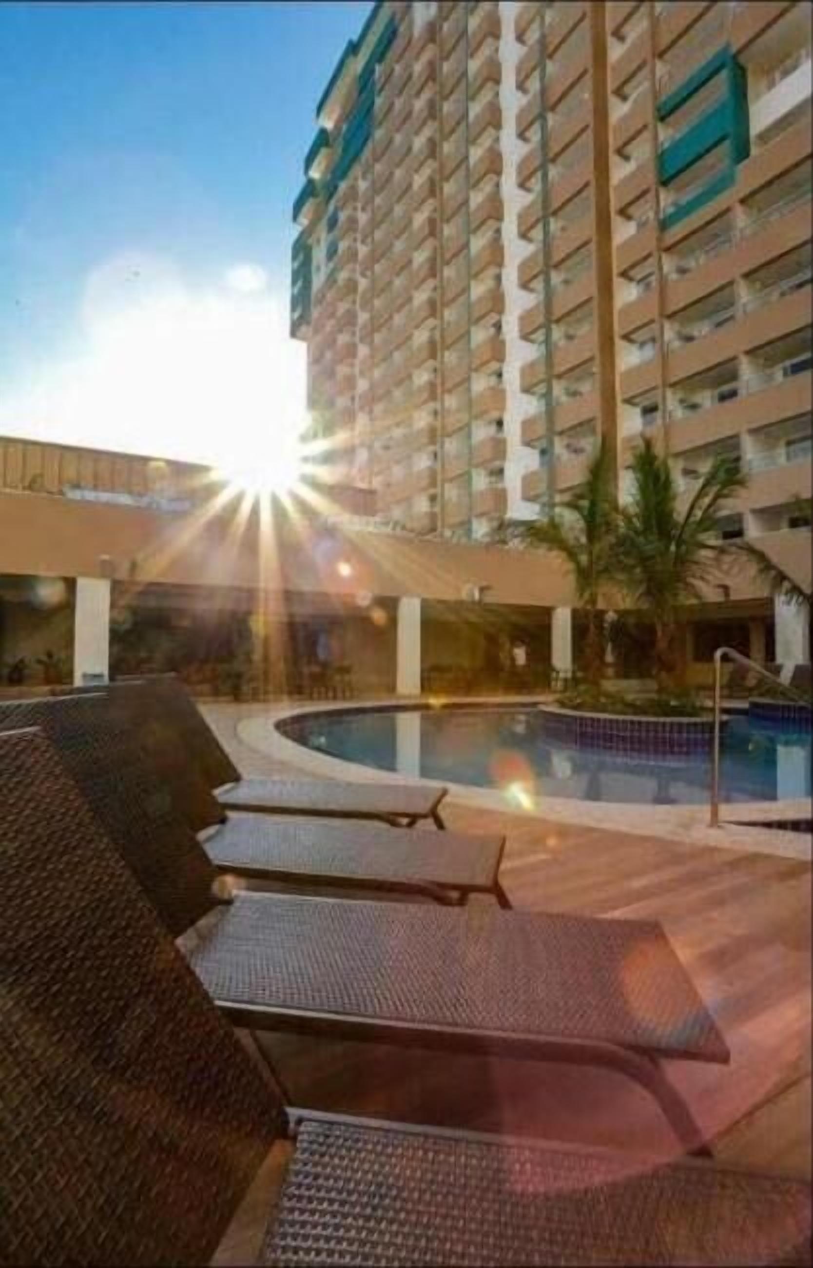A hotel with a pool area, lounge chairs, and a high-rise building in the background.