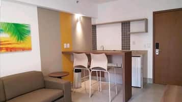 Um espaço compacto para viver, com sofá, pequena mesa de jantar para duas pessoas, cozinha compacta e uma porta.