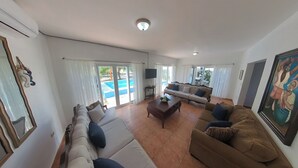 En rummelig stue med en stor sofa, en mindre sofa og et sofabord. Der er et fjernsyn på et stativ, og et billede på væggen.