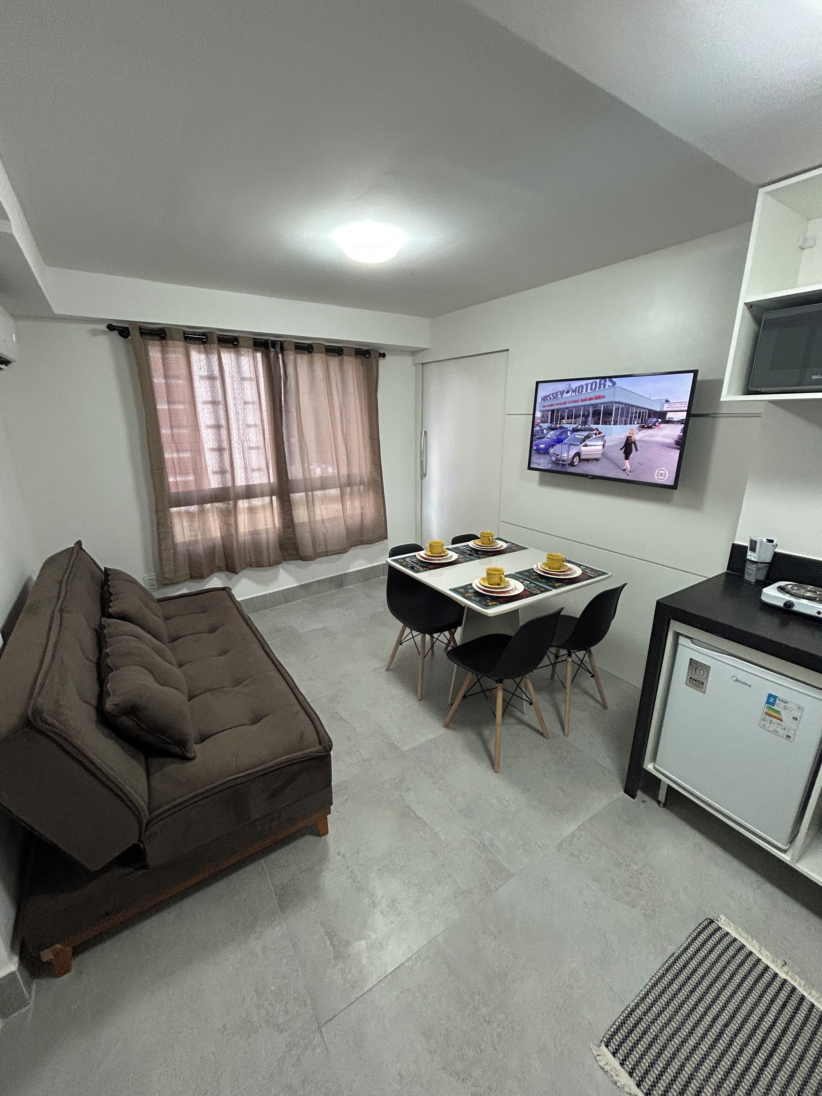 Un espace de vie compact comprenant un canapé, une table à manger avec des chaises, une petite kitchenette et un téléviseur fixé au mur.