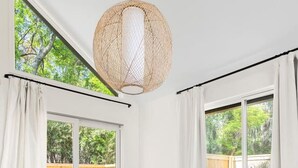 A dining area with a wooden table, white chairs, and a woven pendant light. - Renovated! Coastal 3 Bedroom in the Heart of MTP (Mount Pleasant)