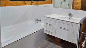 A bathroom with a wooden ceiling, a white bathtub, a vanity with a mirror, and a shower area. - Experience nature at it's finest! (Pukekohe)