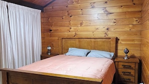 A wooden-paneled bedroom with a bed, a nightstand, and a hanging light fixture. - Experience nature at it's finest! (Pukekohe)