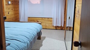 A wooden-paneled room with a bed, a window with curtains, and a door. - Experience nature at it's finest! (Pukekohe)