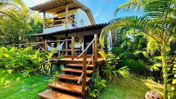 A two-story wooden house with a balcony, surrounded by lush greenery and a hammock. - Casa da Primavera (Porto Seguro)