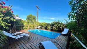A wooden deck with a swimming pool, lounge chairs, and a wooden fence. - Casa da Primavera (Porto Seguro)