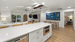 A modern kitchen with a central island, built-in oven, and a dining area with a wooden table and chairs. - Lush Oasis w/ Heated Pool & Fire Pit (Naples)