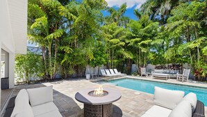 A poolside area with a fire pit, lounge chairs, and a swimming pool surrounded by trees. - Lush Oasis w/ Heated Pool & Fire Pit (Naples)