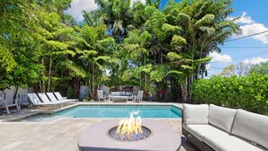 A pool area with a fire pit, lounge chairs, and a sofa. - Lush Oasis w/ Heated Pool & Fire Pit (Naples)