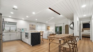 A modern kitchen with white cabinetry, a wooden dining table, and a central island. - Lush Oasis w/ Heated Pool & Fire Pit (Naples)