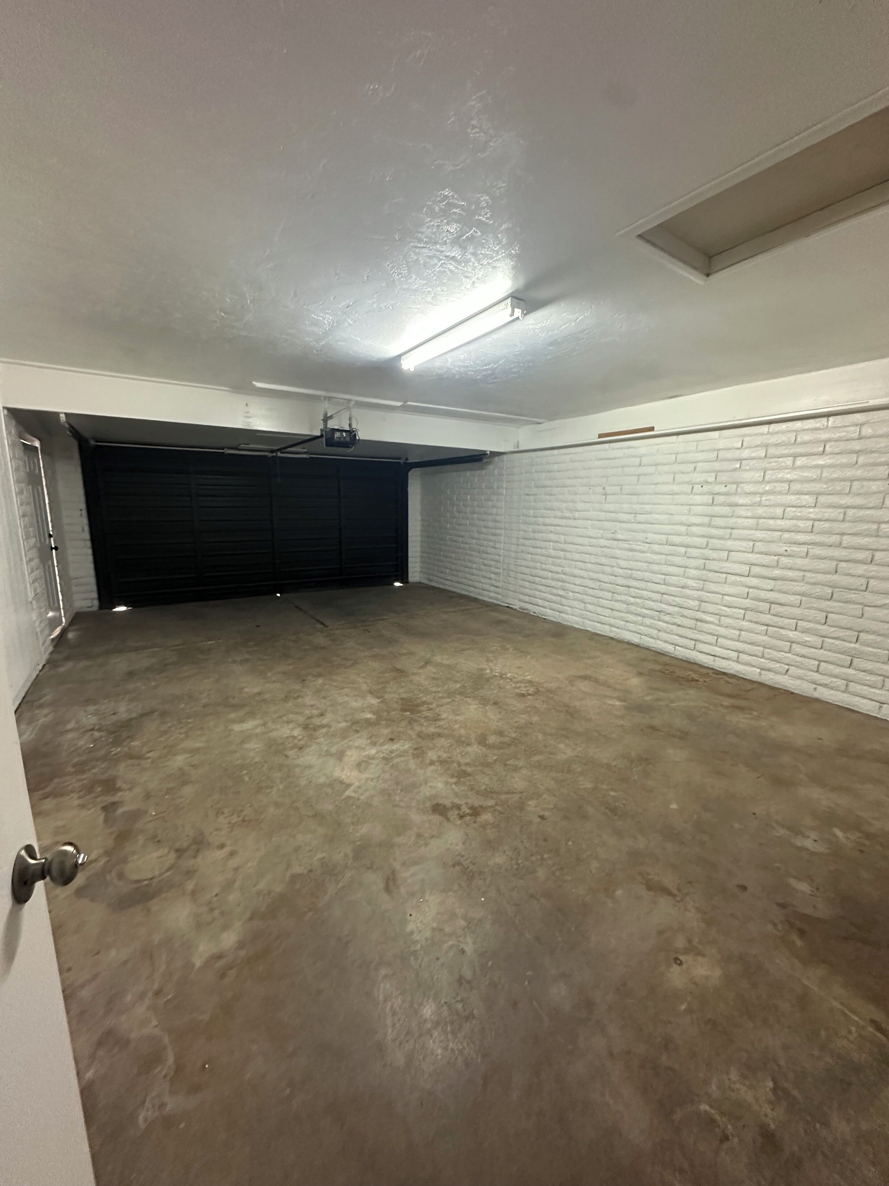 A garage with a concrete floor, a black garage door, and a white brick wall.