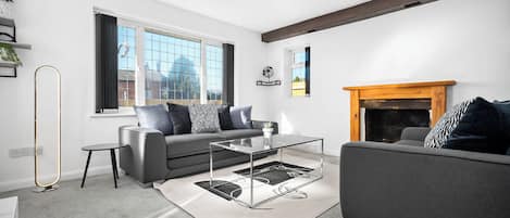 Een moderne woonkamer met een grijze bank, een glazen salontafel en een open haard.