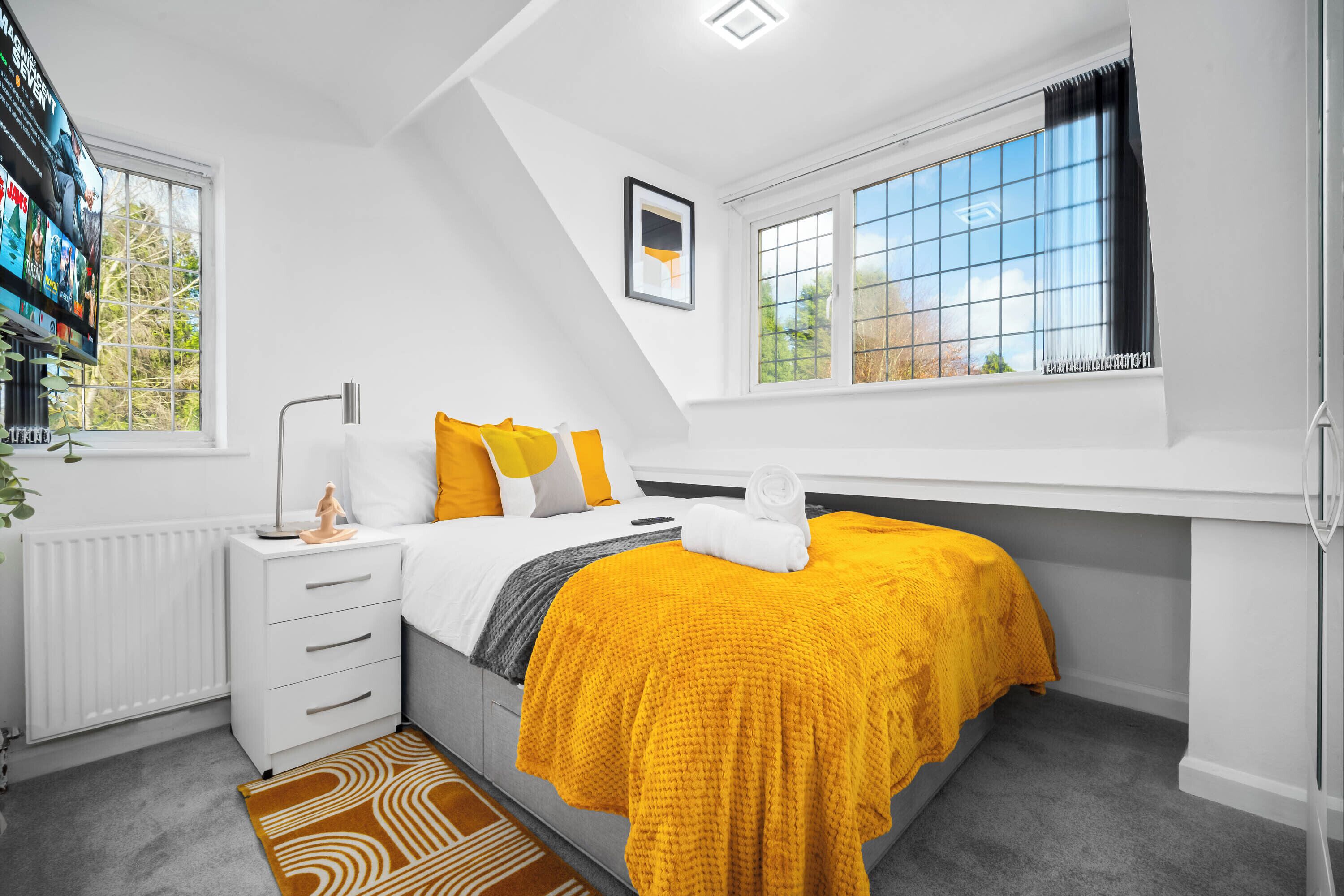 A bedroom with a bed, a nightstand, a radiator, a window, and a TV on the wall.