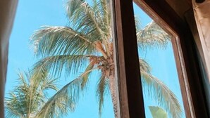 A view through a window with wooden frames, displaying tall palm trees against a clear blue sky. - Vai Dá Certo Pousada  (Jijoca de Jericoacoara)
