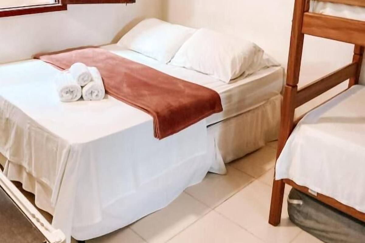 A bedroom with a bed, a bedside table, a wooden headboard, and a window with blinds.