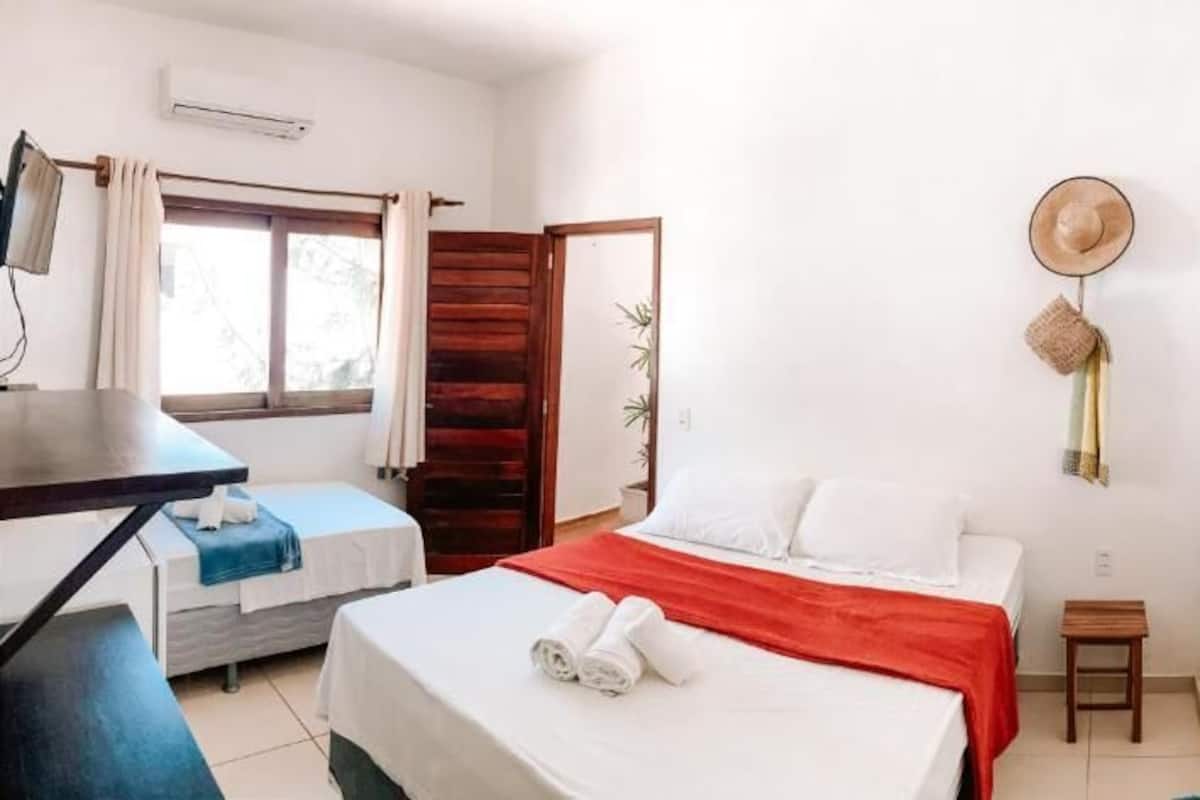 A hotel room with two beds, a desk, a chair, a small table, and a mirror.