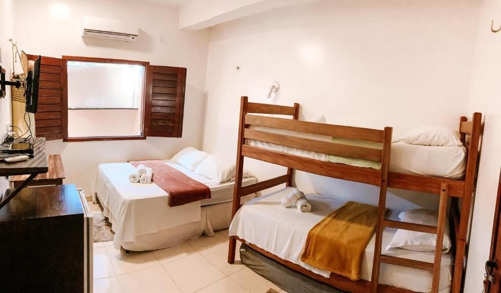 Una habitación con dos camas individuales, un escritorio con silla, aire acondicionado y una ventana con contraventanas de madera.