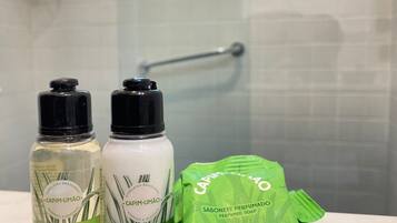 Deux flacons de shampoing et d’après-shampoing Capim-Limão, et un sac vert contenant du savon L’OCCITANE AU BRASIL, posés sur le comptoir d’une salle de bain.