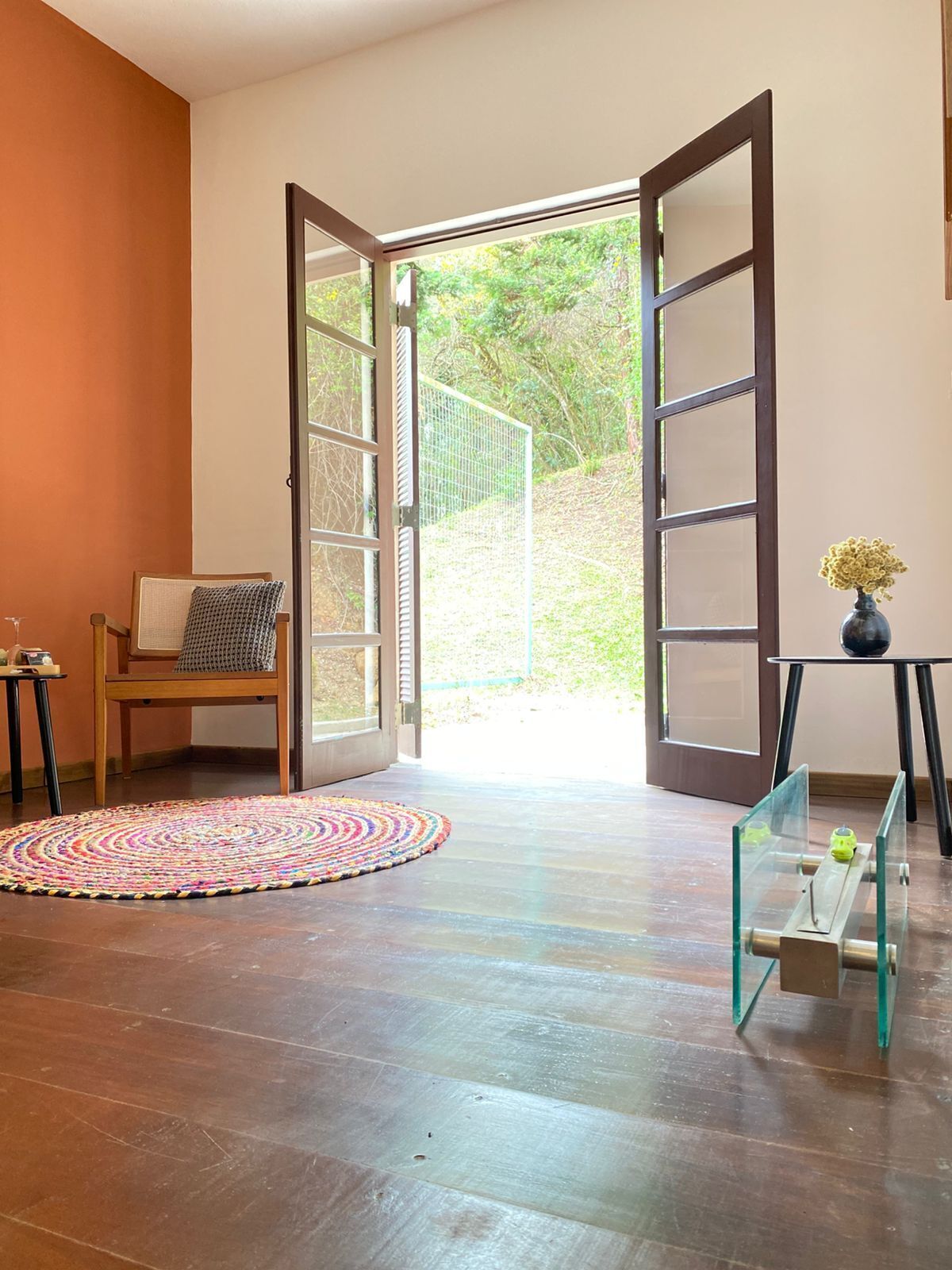 An open door leading to a garden, a wooden chair, a colorful rug, and a glass table with a vase.
