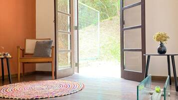 An open door leading to a garden, a wooden chair, a colorful rug, and a glass table with a vase.