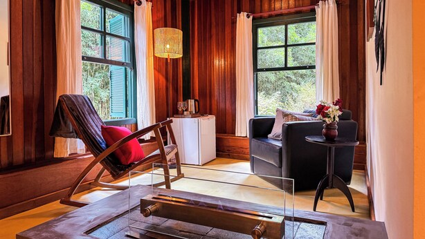 A wooden room with a glass table, a rocking chair, a sofa, and a small table with a vase. - Pousada Barra do Bié (Cunha)