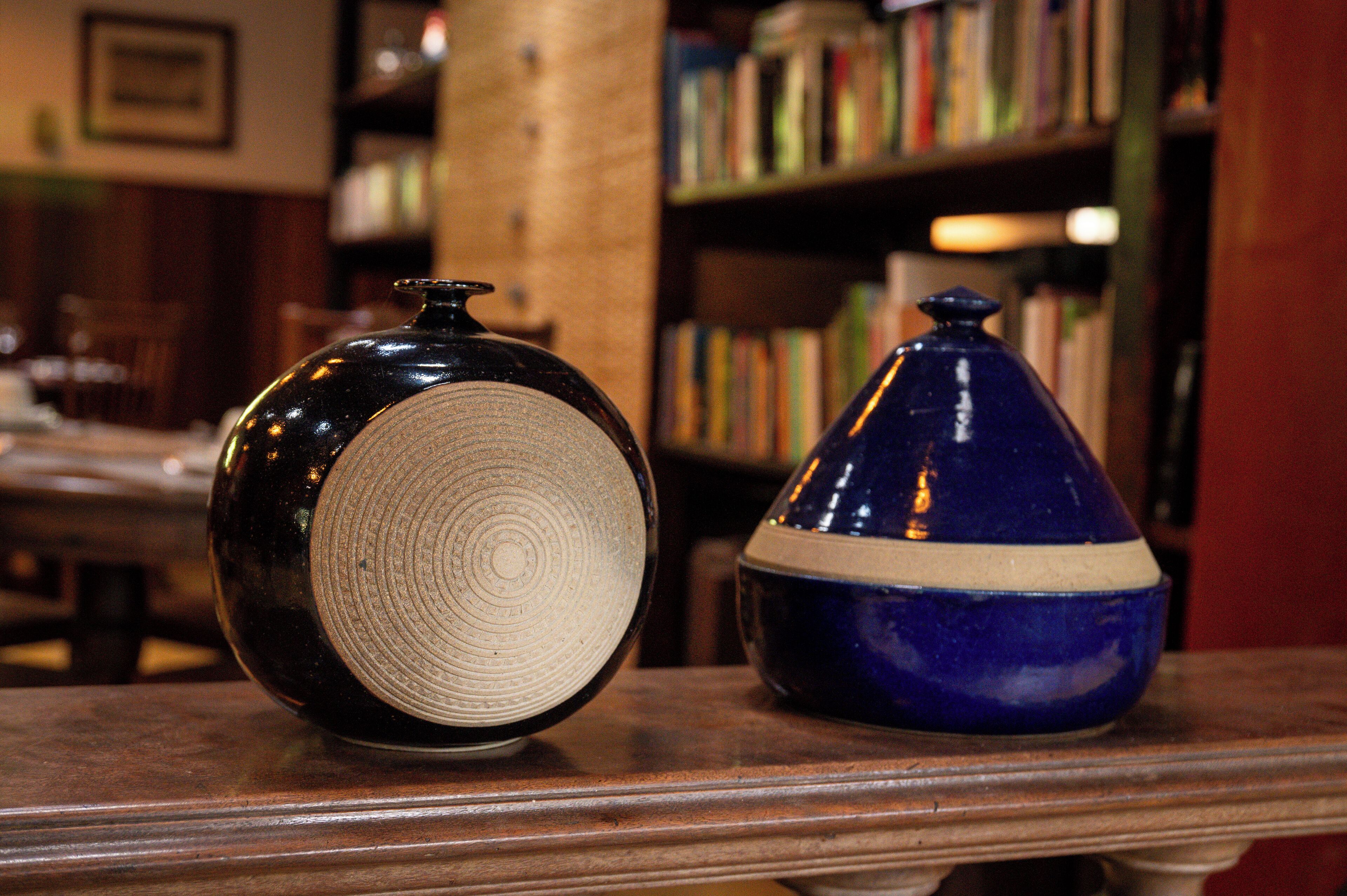 Two ceramic vases on a wooden table with a bookshelf in the background.
