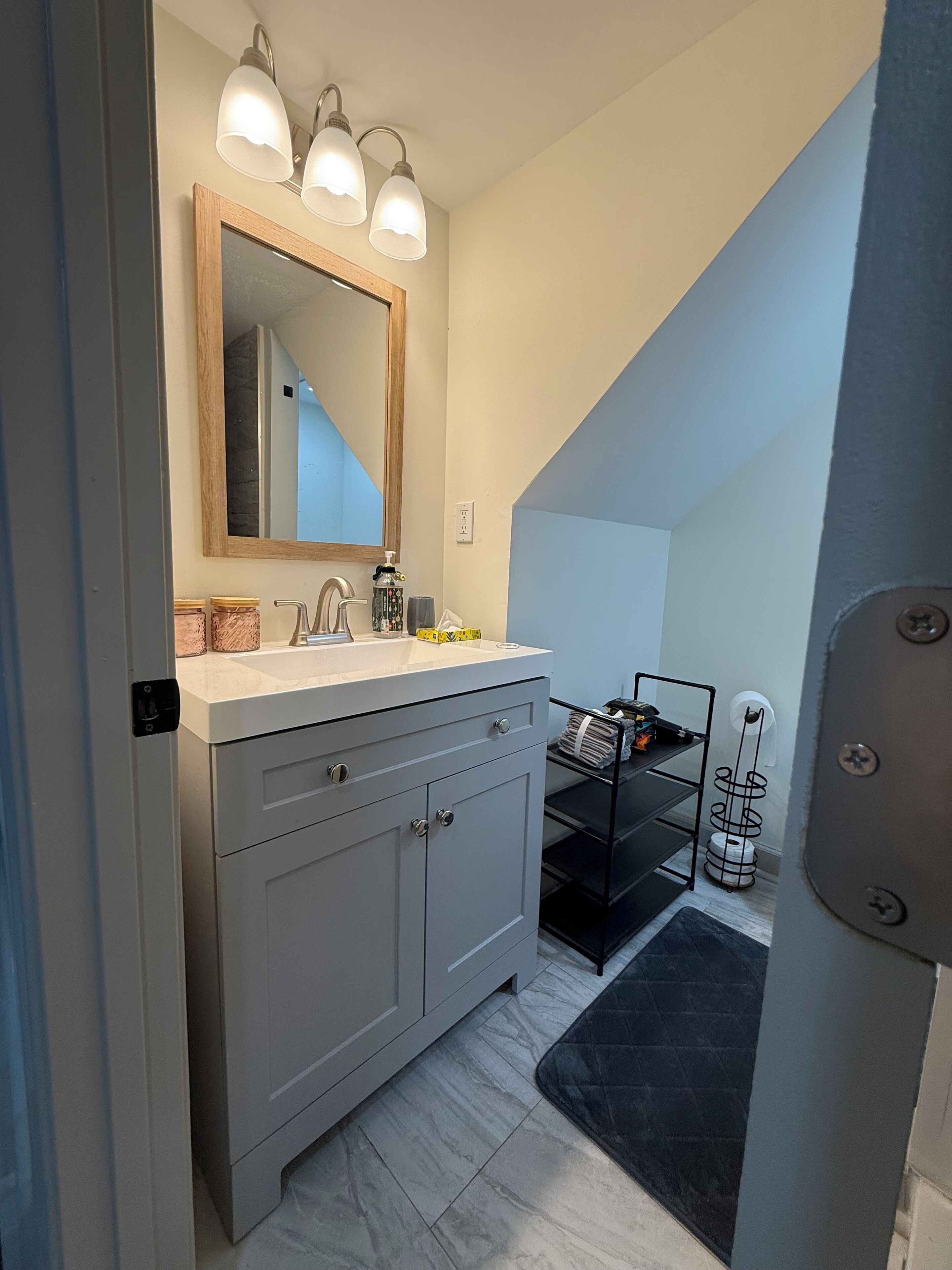 A bathroom with a white vanity, a mirror with three lights, and a towel rack.