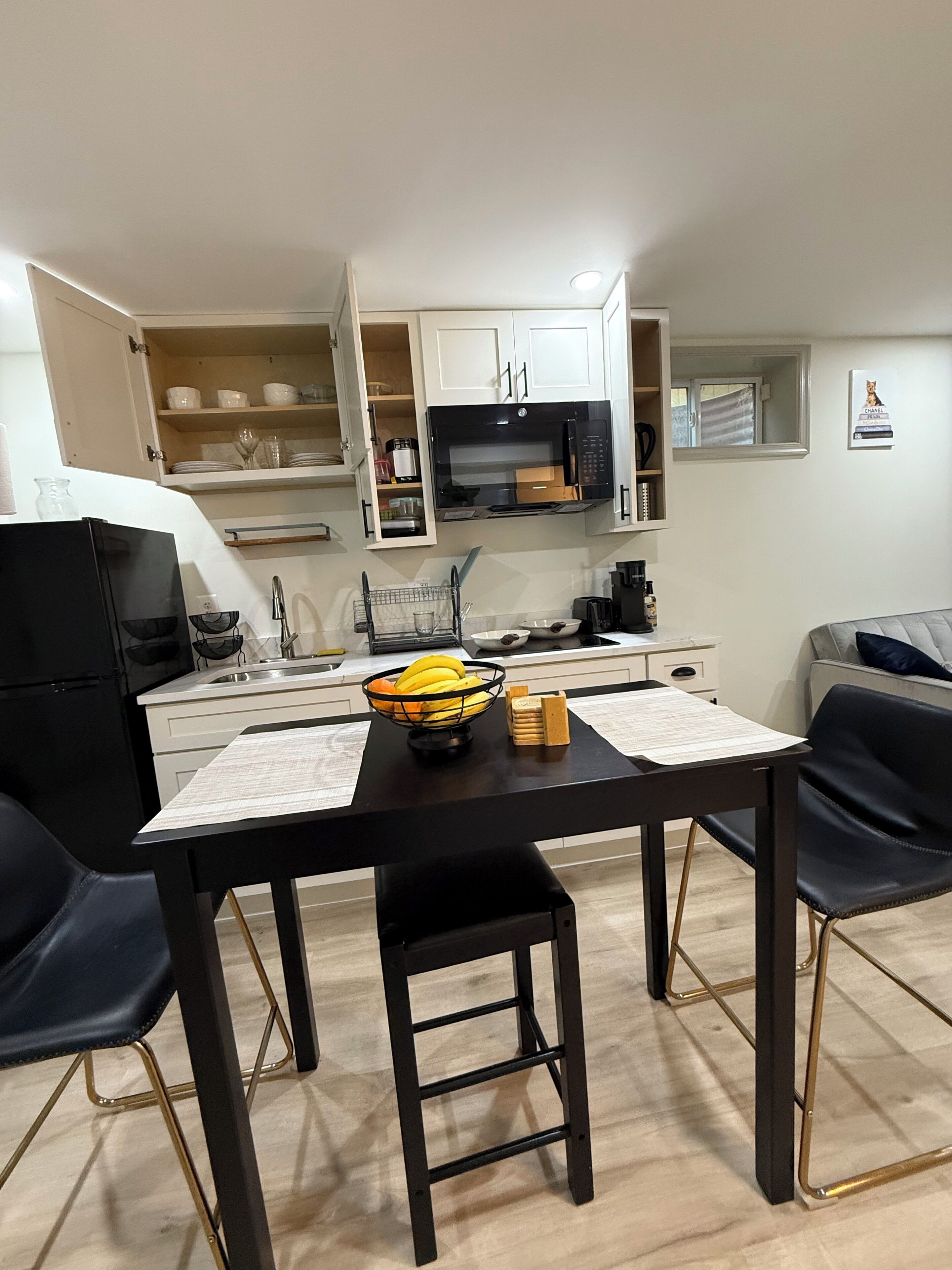 A compact kitchen with white cabinets, a black countertop, and a dining area with black chairs.