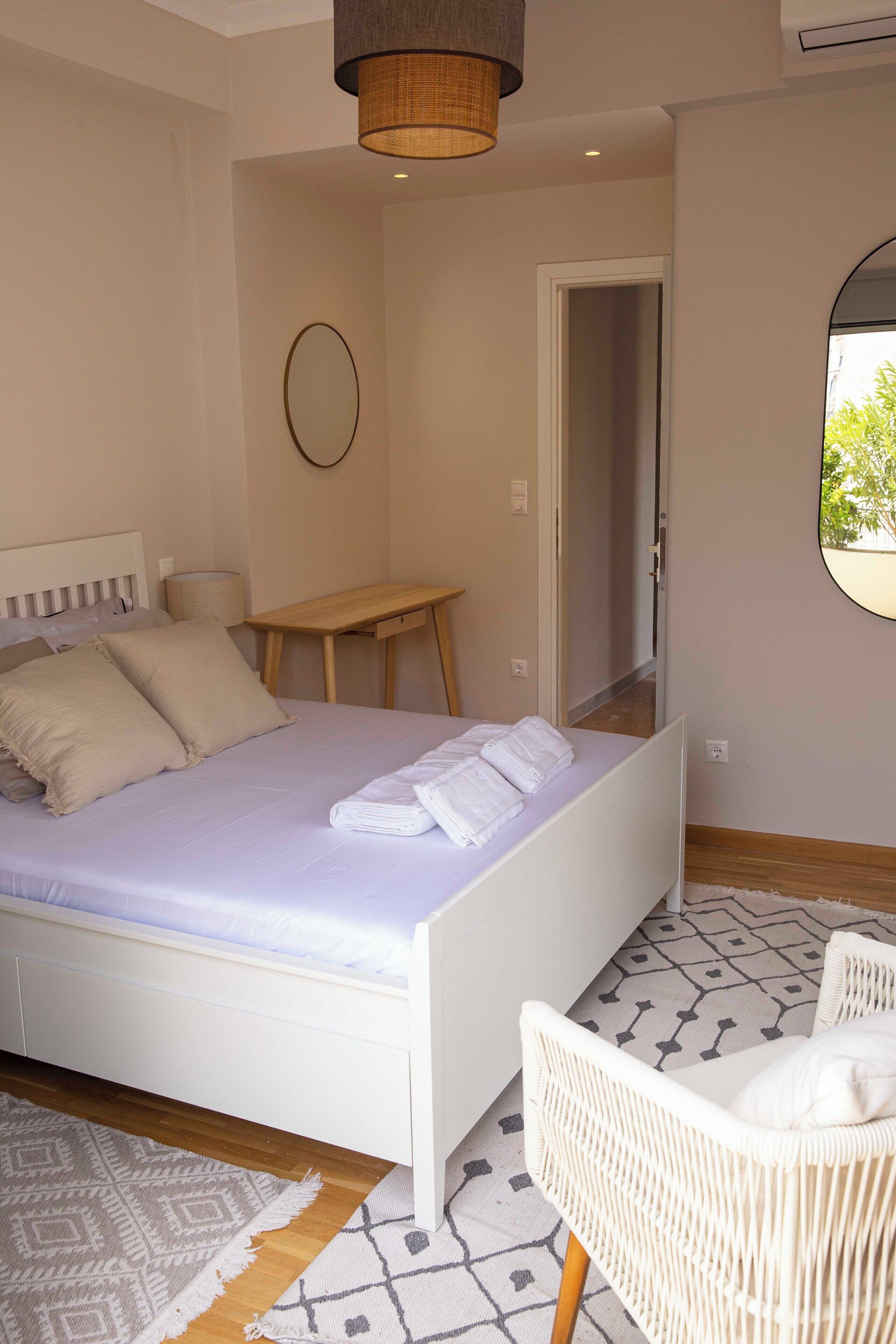A bedroom with a bed, a chair, a table, and a mirror.