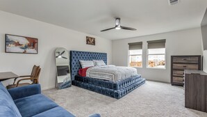 Une chambre à coucher avec un lit doté d’une tête de lit capitonnée, un canapé recouvert d’un tissu bleu, un bureau et une commode.