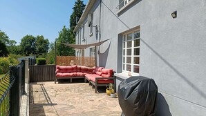 Un'area patio coperta con un divano componibile rosso, una griglia barbecue e un pavimento in pietra.