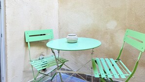A small outdoor seating area with a round table and two green chairs, set against a textured wall. - L'écrin Bleu - Studio Cosy Intra-Muros (Lunel)