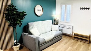 A modern living room with a grey sofa, a wooden floor, a teal accent wall, and a small table with a chair. - L'écrin Bleu - Studio Cosy Intra-Muros (Lunel)