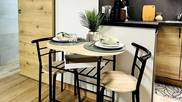 A modern kitchen with a wooden table, black chairs, and a clock on the wall. - L'écrin Bleu - Studio Cosy Intra-Muros (Lunel)