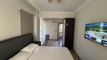 A bedroom with a bed, a TV mounted on the wall, and a door leading to another room.
