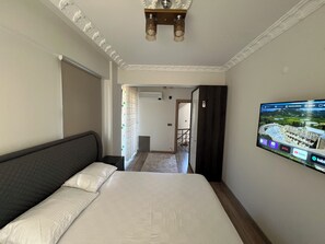 A bedroom with a bed, a TV mounted on the wall, and a door leading to another room. - Beşer Turizm - Avşa Adası Çınar Koyu (Marmara)