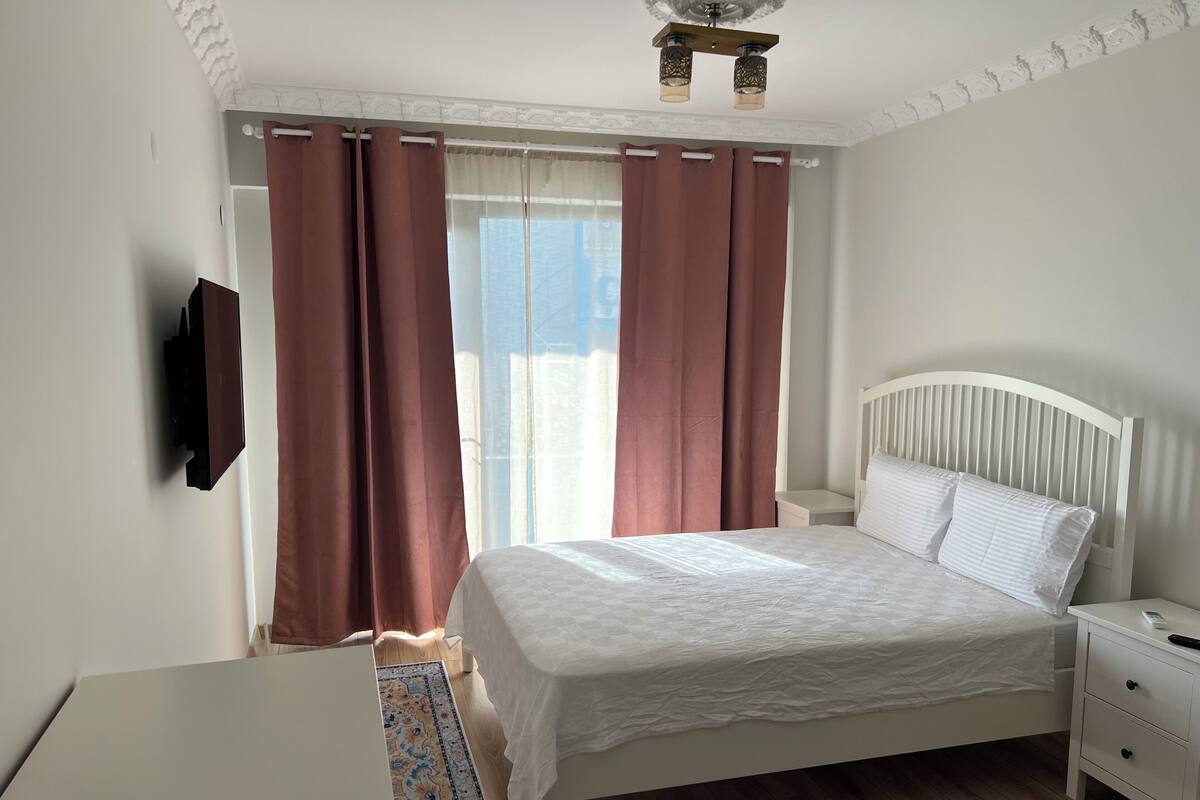 A bedroom with a bed, nightstand, and a TV mounted on the wall.