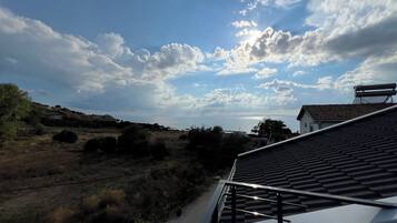 A view of a coastal landscape with a clear sky, a distant body of water, and a building with a tiled roof.