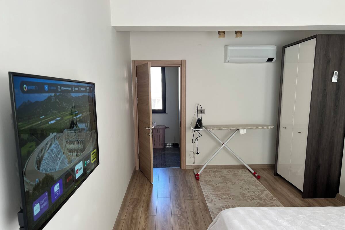 A hotel room with a bed, a TV mounted on the wall, a wardrobe, and a small ironing station.