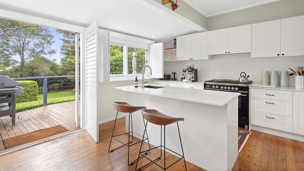Una cocina moderna con armarios blancos, una isla grande con taburetes, una estufa a gas y vista al patio trasero.