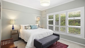 Un dormitorio con cama, mesitas de noche, un banco y una ventana con persianas.