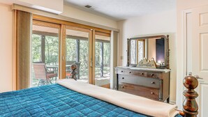 Ein Schlafzimmer mit einem großen Bett, einem Schminktisch und einem Spiegel. Eine Glastür führt zu einem Außenbereich mit einem Stuhl und einem Tisch.