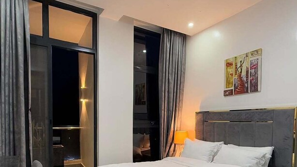 Ein modernes Schlafzimmer mit Bett, Schreibtisch und Stuhl. Eine Schiebetür führt zu einem Balkon.