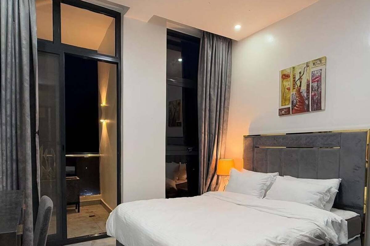 A modern bedroom with a bed, a desk, and a chair. There is a sliding door leading to a balcony.