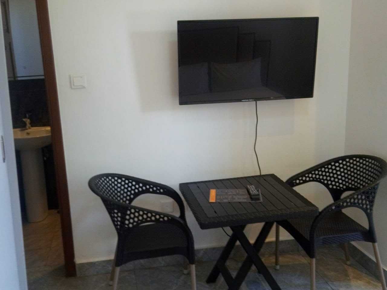 A small room with a TV mounted on the wall, a table with two chairs, and a small sink in the corner.