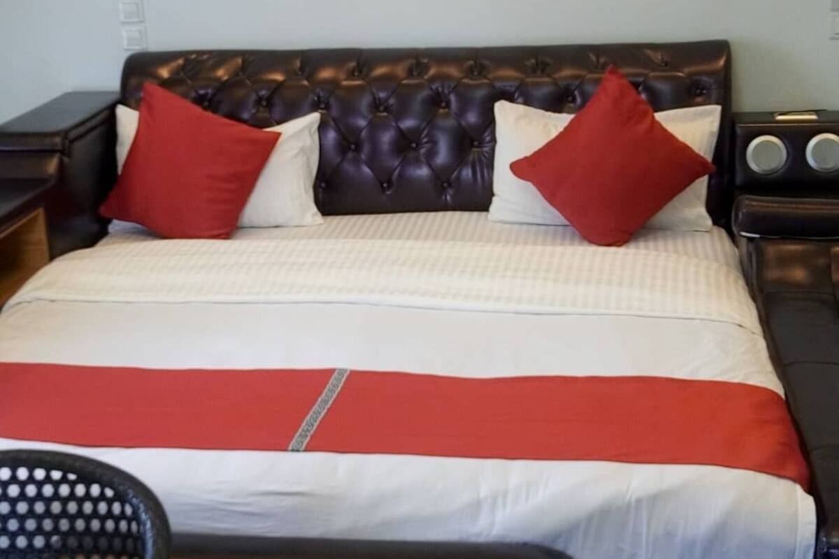 A bed with a tufted headboard, red and white bedding, and a red accent strip.